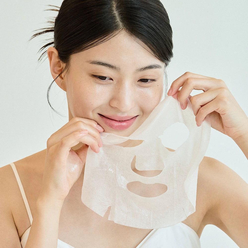 Vrouw houdt gezichtsmasker vast. Masker met openingen voor ogen, neus en mond. Vrouw glimlacht.