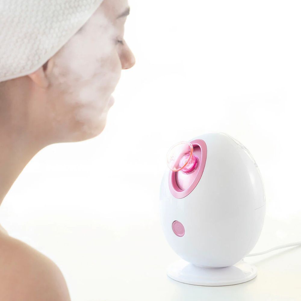 Appareil ovale blanc avec accents roses. Une personne avec une serviette sur le visage. De la vapeur s'élève.