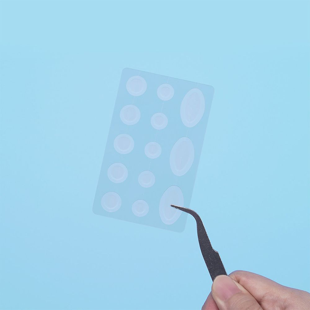 Patchs transparents pour boutons sur une feuille. Différentes tailles et formes. Une pince à épiler saisit un patch.