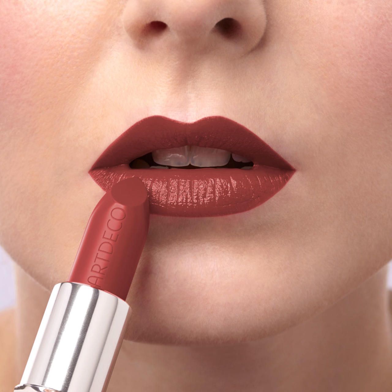 Persoon brengt rode lipstick aan. Lipstick met ARTDECO-opschrift.
