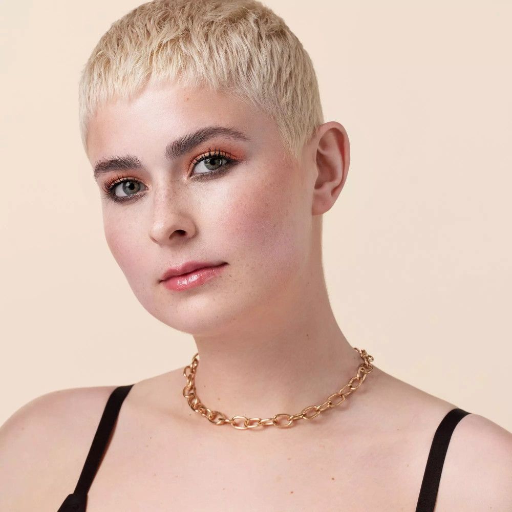 Portret van een vrouw met blond haar en een gouden halsketting.