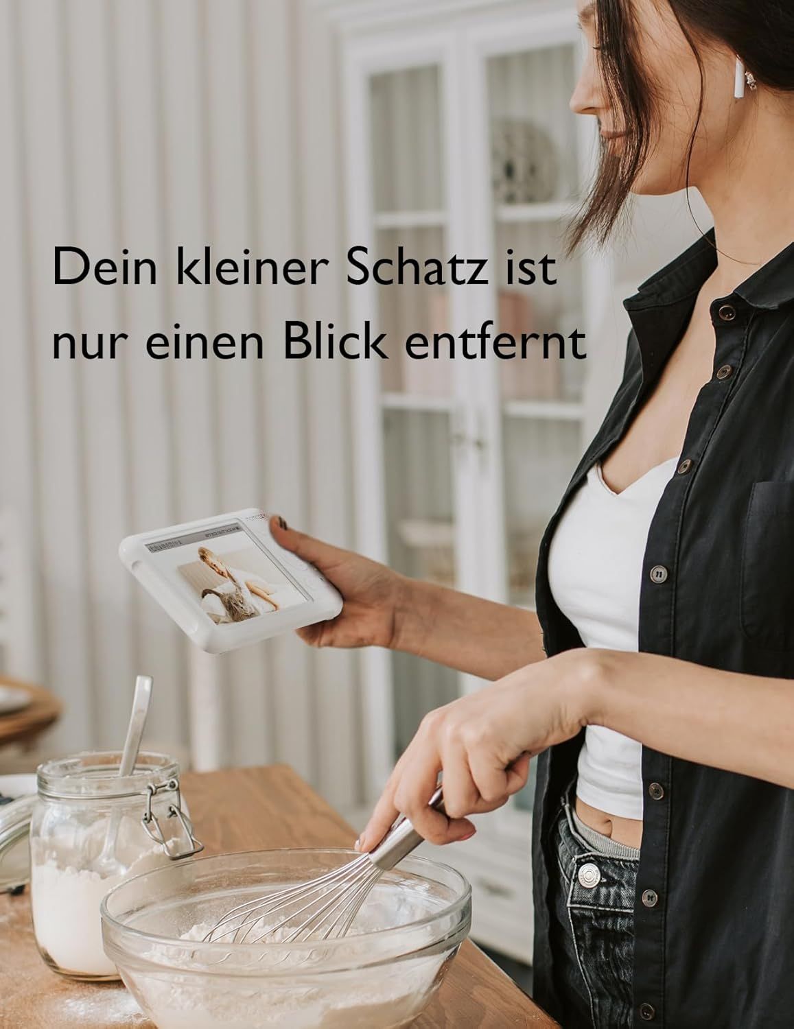 Femme tenant un écran de babyphone avec une image de bébé dans la cuisine.
