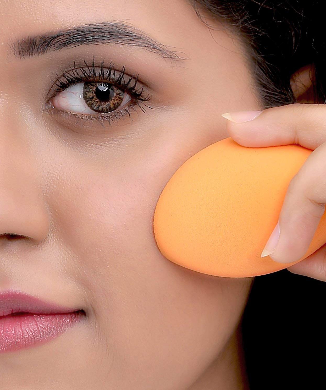 Éponge de maquillage orange, de forme ovale, tenue par une main.