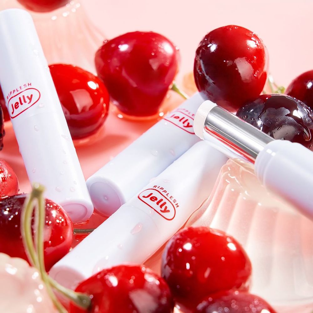 Plusieurs bâtons de baume à lèvres blancs avec logo rouge, entourés de cerises. Certains bâtons sont ouverts.