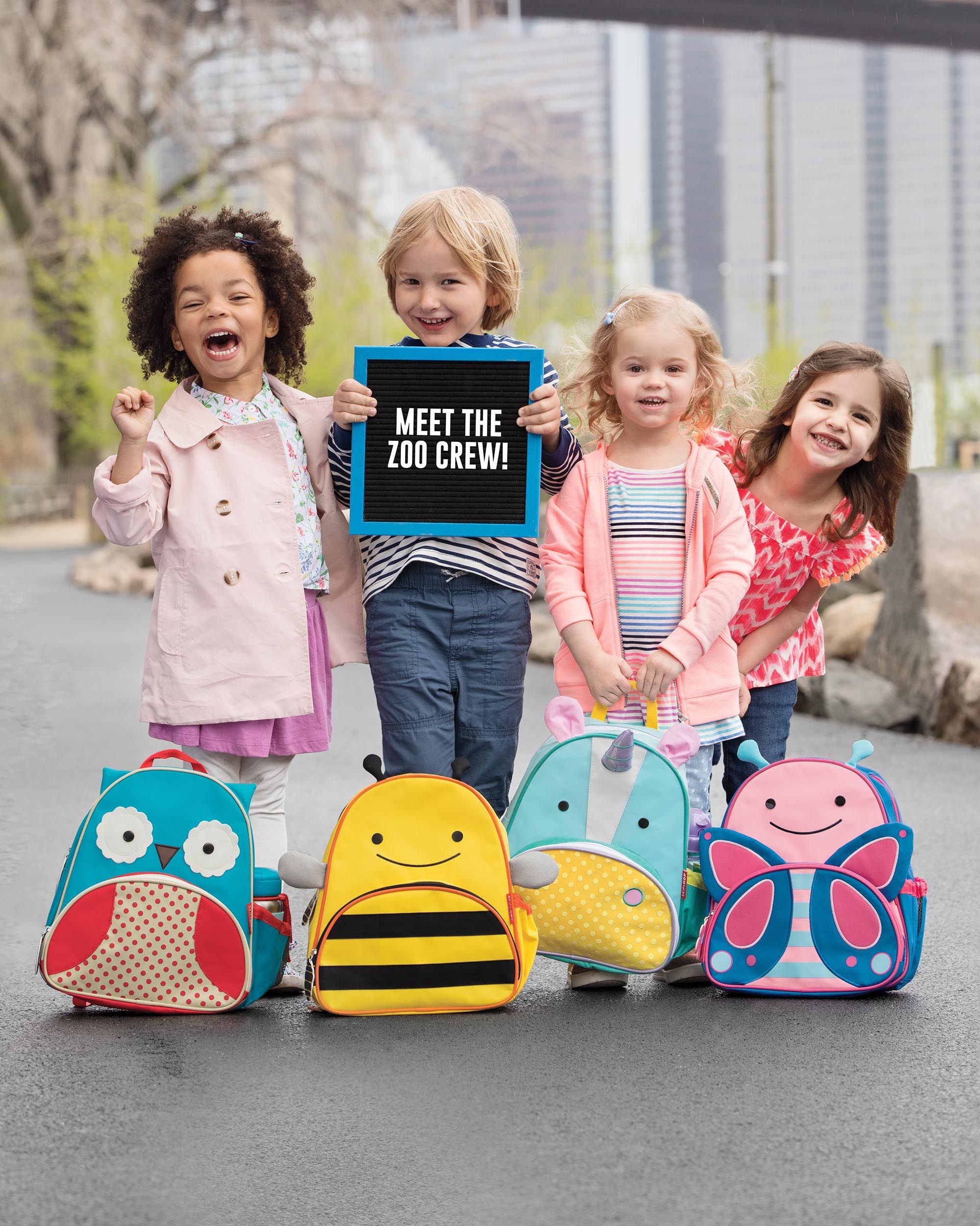 Kinderen met verschillende dierenrugzakken. Eenhoorn, bij, uil, vlinder. Bord: Meet the Zoo Crew!