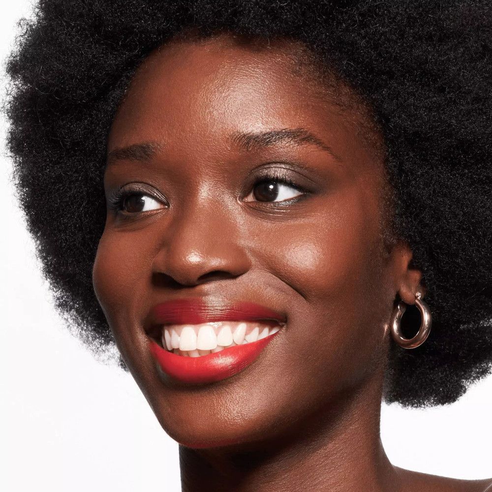 Portrait d'une femme à la peau foncée. Elle porte du rouge à lèvres rouge et des créoles dorées.