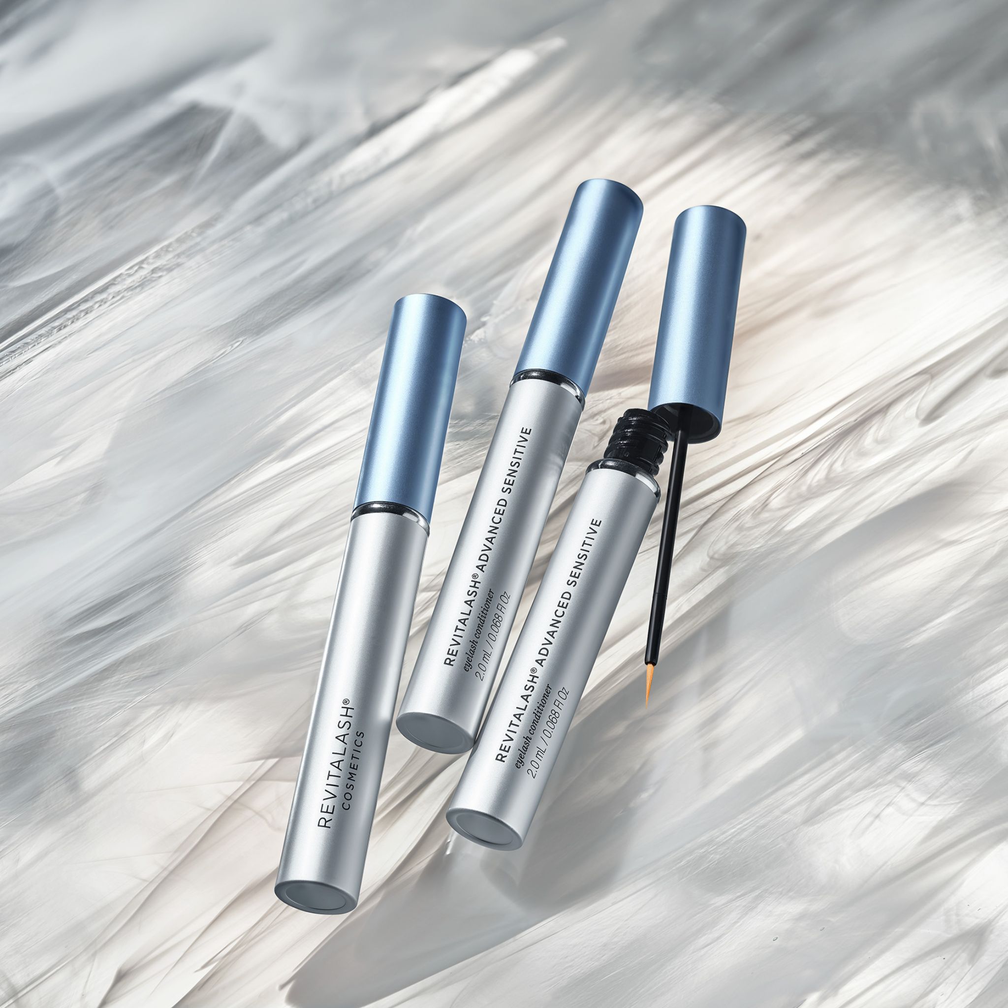Drie RevitaLash® Advanced Sensitive flacons, één met open applicator, op witte achtergrond.
