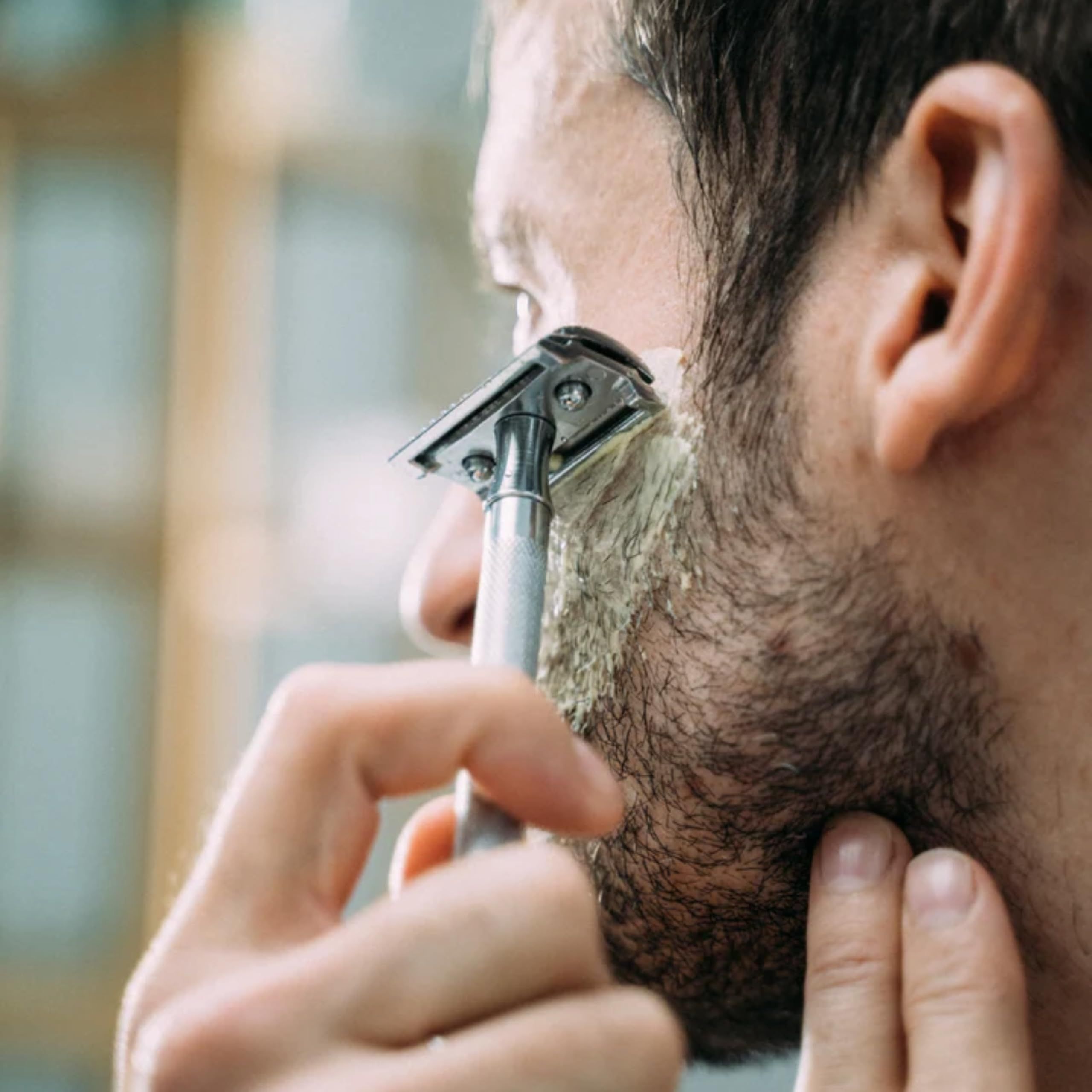 Gros plan d'une personne qui se rase. Un rasoir est utilisé pour enlever la mousse de la joue.