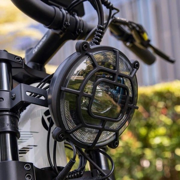 Phare de vélo rond avec grille de protection. Boîtier noir, lentille claire. Fixé sur la fourche.