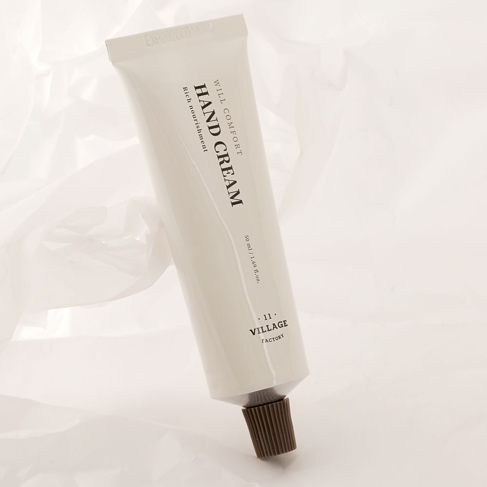 Crèmetube met tekst HAND CREAM, WILL COMFORT, VILLAGE FACTORY. Beige tube op witte achtergrond.