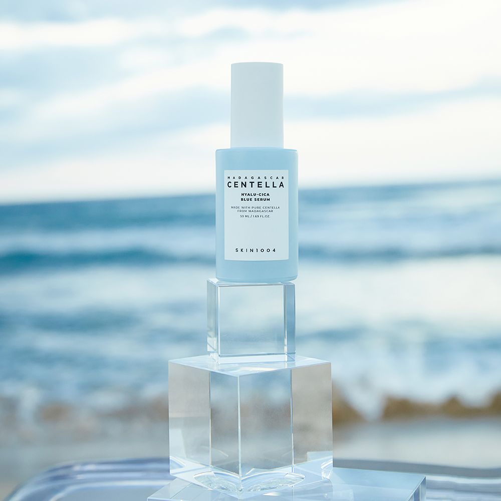 Flacon de sérum bleu clair sur cubes de verre devant fond marin. Inscriptions : MADAGASCAR CENTELLA, HYALU-CICA BLUE SERUM, SKIN1004.