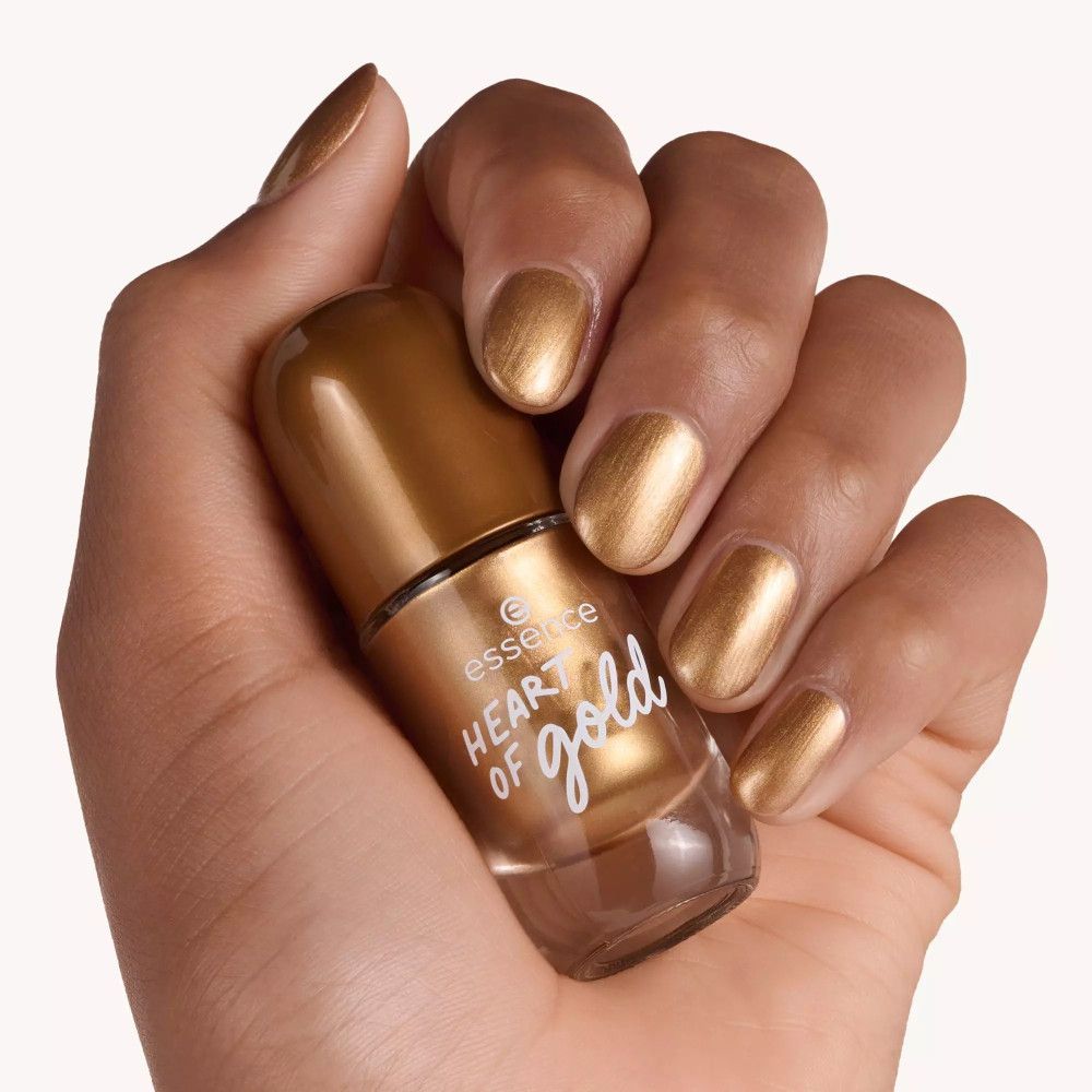 Main avec ongles vernis dorés. Tient un flacon de vernis à ongles. Inscription : Heart of Gold.