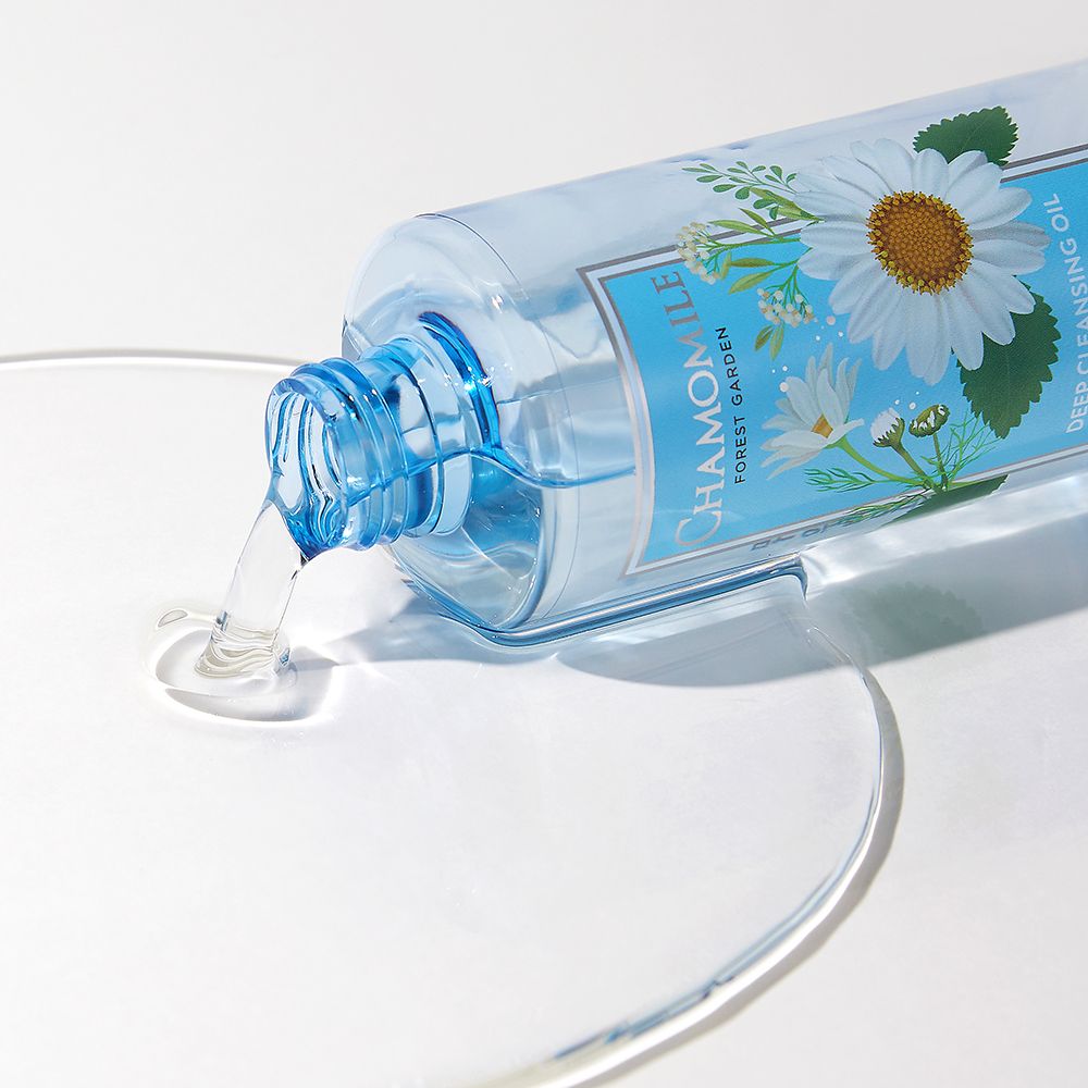 Transparante fles met kamille-etiket, liggend. Vloeistof stroomt eruit. Opschrift: CHAMOMILE, FOREST GARDEN, DEEP CLEANSING OIL, NATURE REPUBLIC.