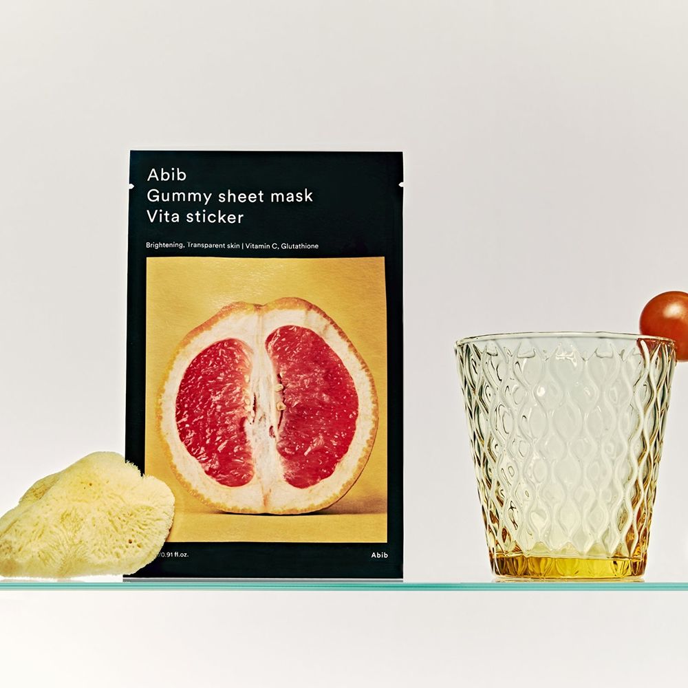 Zwarte verpakking met productnaam en afbeelding van grapefruit. Naast: glas, spons. Tekst: Gummy sheet mask Vita sticker.