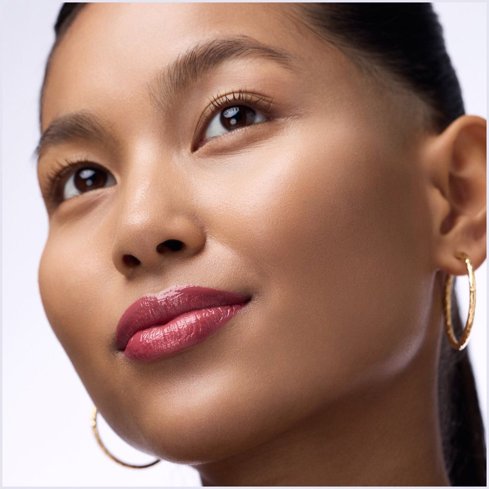 Portrait d'une femme avec des lèvres maquillées avec un plumper à lèvres rouge. Boucles d'oreilles dorées.