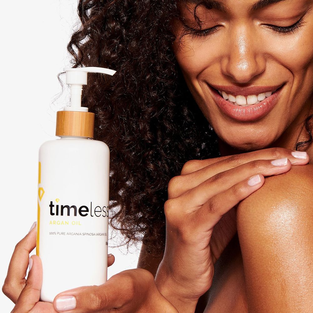 Vrouw houdt een flesje timeless Argan Oil vast. Fles met pomp en houten ring. Gele sticker met Pure.