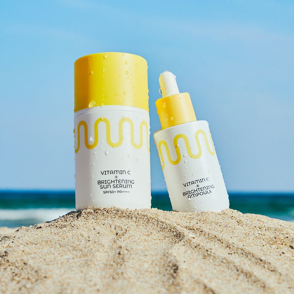 Flacon blanc avec bouchon jaune et motif ondulé, à côté d'un flacon compte-gouttes. Sur la plage.