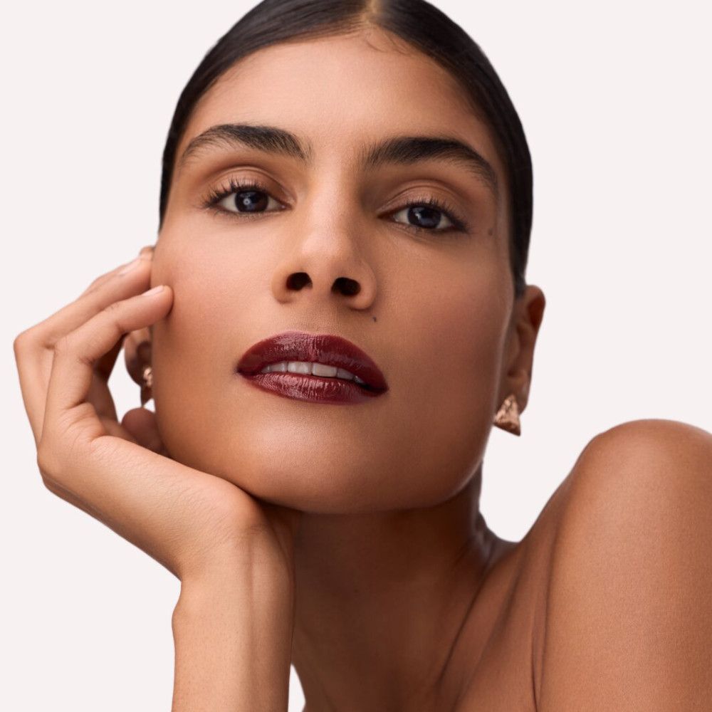 Portret van een vrouw met dieprode Lip Tint op haar lippen. Ze steunt haar kin op haar hand.