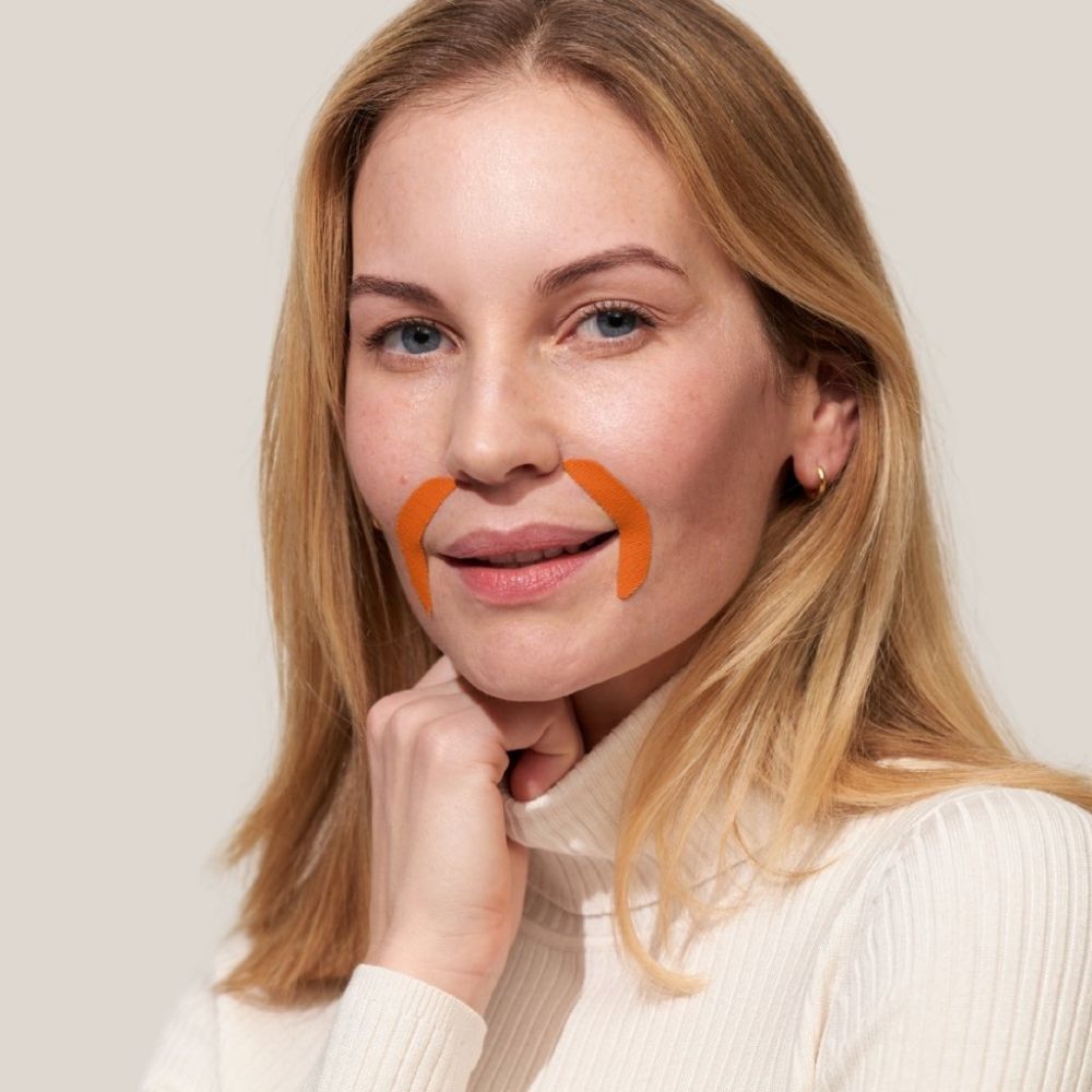 Vrouw met oranje mondpatches. Ze draagt een witte coltrui. Patches op de bovenlip en kin.