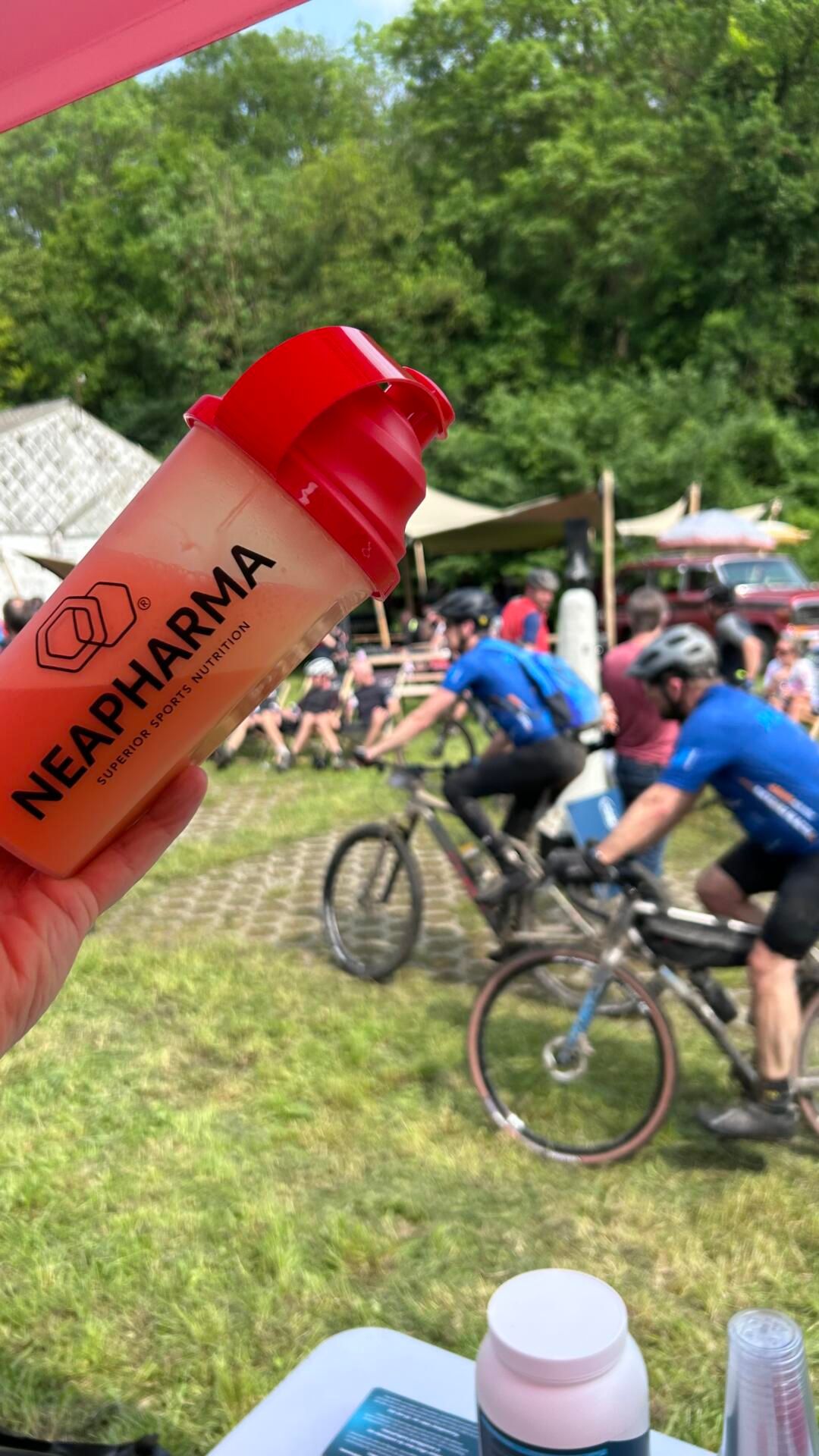 Main tenant un shaker avec liquide orange. Imprimé : Neapharma, Superior Sports Nutrition.