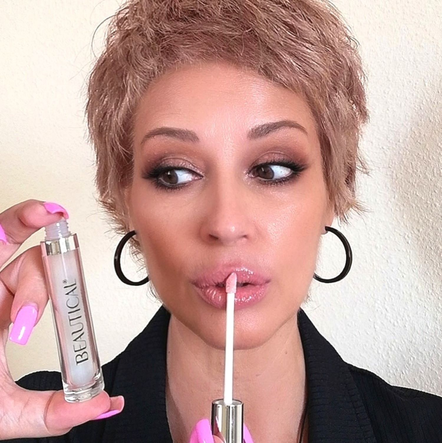 Femme tenant BEAUTICAL Instant Lip Plumper. Elle porte du rouge à lèvres et regarde sur le côté. Boucles d'oreilles noires.