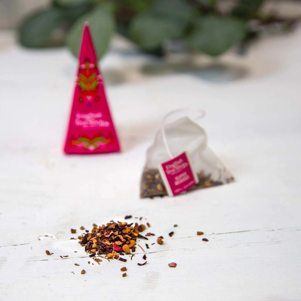 Piramide theezakje en losse thee. Roze piramide theezakje ernaast. Opschrift: English Tea Shop. Losse theebladeren.