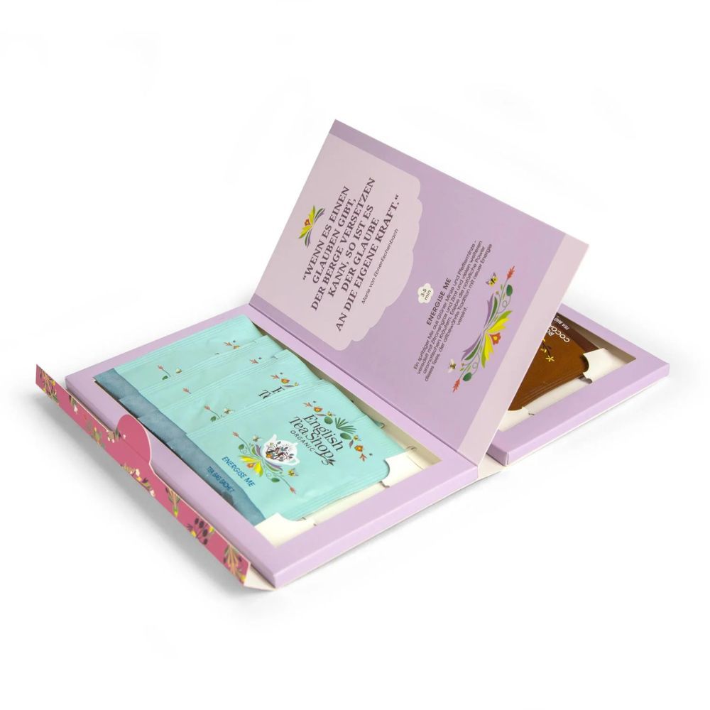 Open cadeaudoos. Theezakjes in lichtblauw en bruin binnenin. Citaat aan de binnenkant van het deksel. Roze rand.