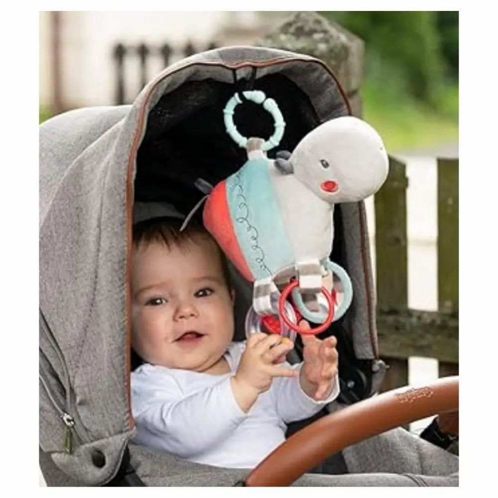 Bébé dans une poussette avec une peluche hippopotame. Le jouet est attaché à la poussette. Bébé sourit.