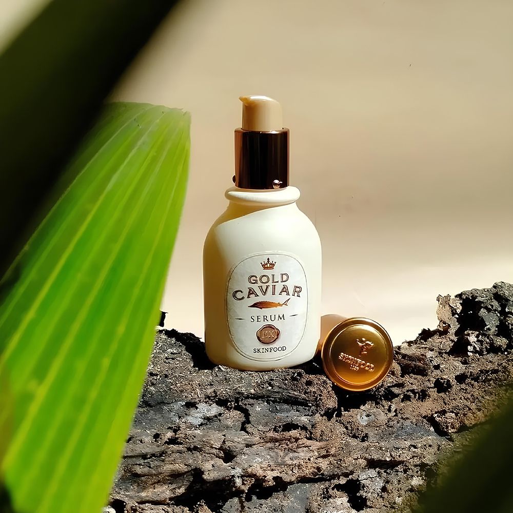 Serumfles met dop en blad. Tekst: Gold Caviar Serum. Merk: SKINFOOD. Achtergrond: hout en bladeren.