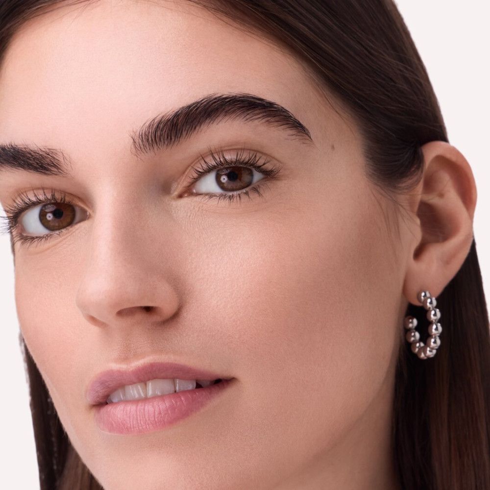 Gros plan sur une femme aux yeux marron clair et boucles d'oreilles. Les boucles sont des créoles à billes argentées.