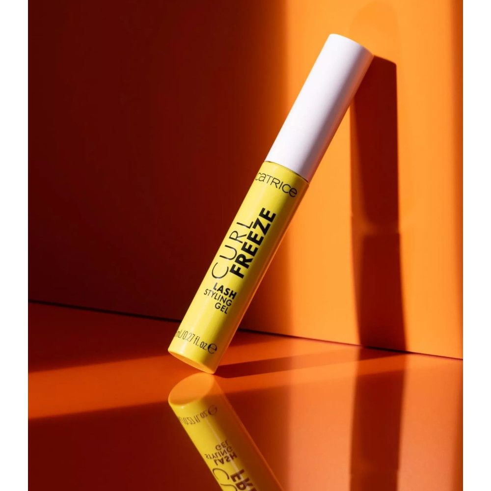 Gele gel tube met tekst 'CURL FREEZE' en 'LASH STYLING GEL'. Witte dop. Op oranje achtergrond, reflectie.