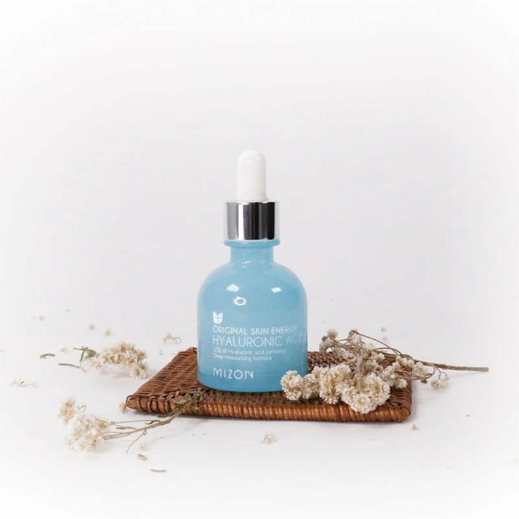 Flacon bleu clair avec bouchon argenté et pipette sur plateau avec fleurs séchées. Inscription : Hyaluronic Acid 100. Marque Mizon.