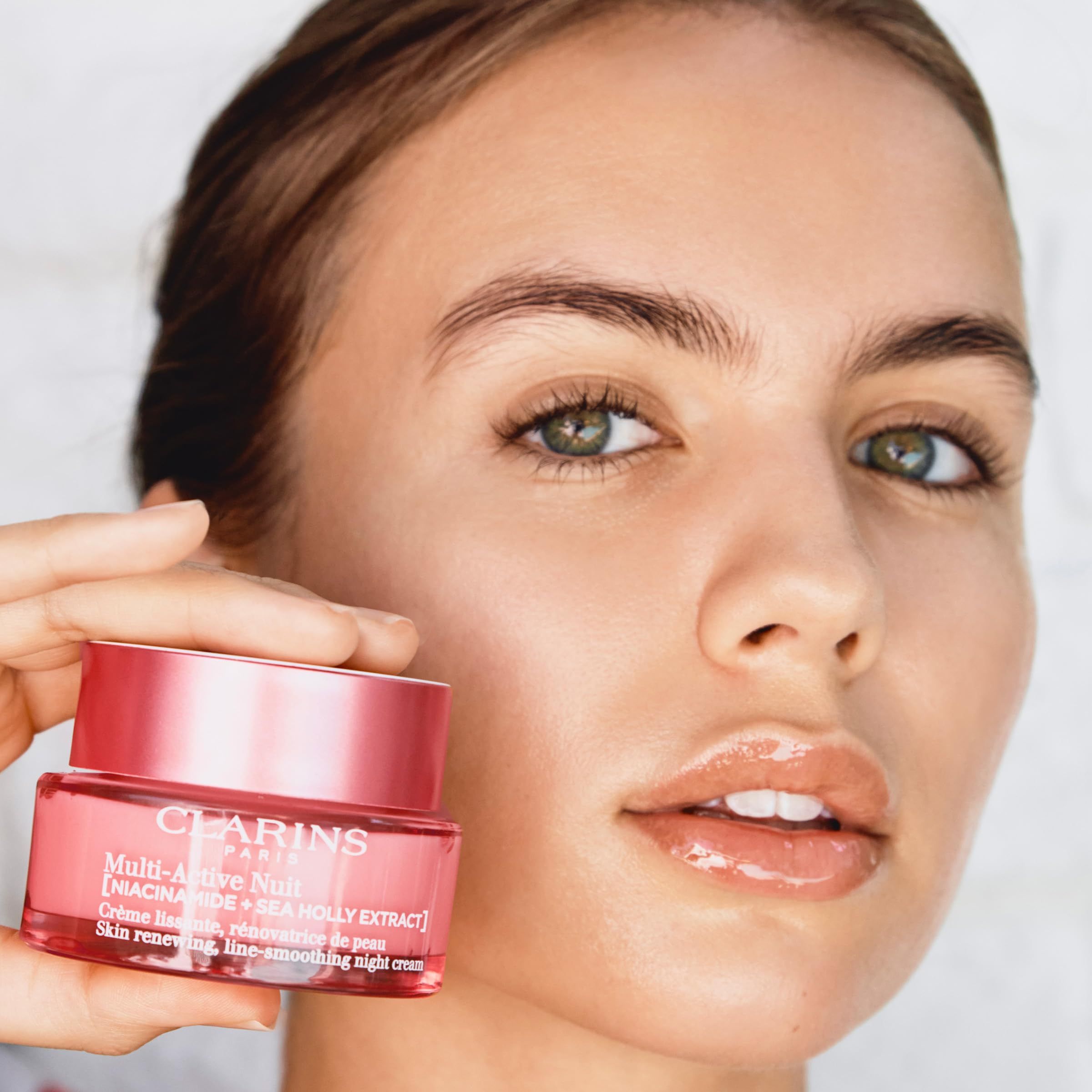 Vrouw houdt roze crème pot vast. Opschrift: CLARINS PARIS, Multi-Active Nuit. Tekst: Skin renewing, line-smoothing night cream.