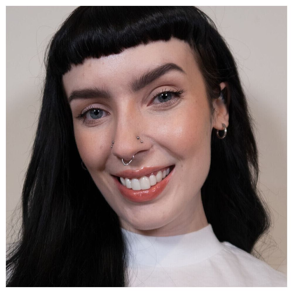 Portrait d'une femme maquillée. Elle sourit. Peau claire, cheveux foncés, sourcils, rouge à lèvres.