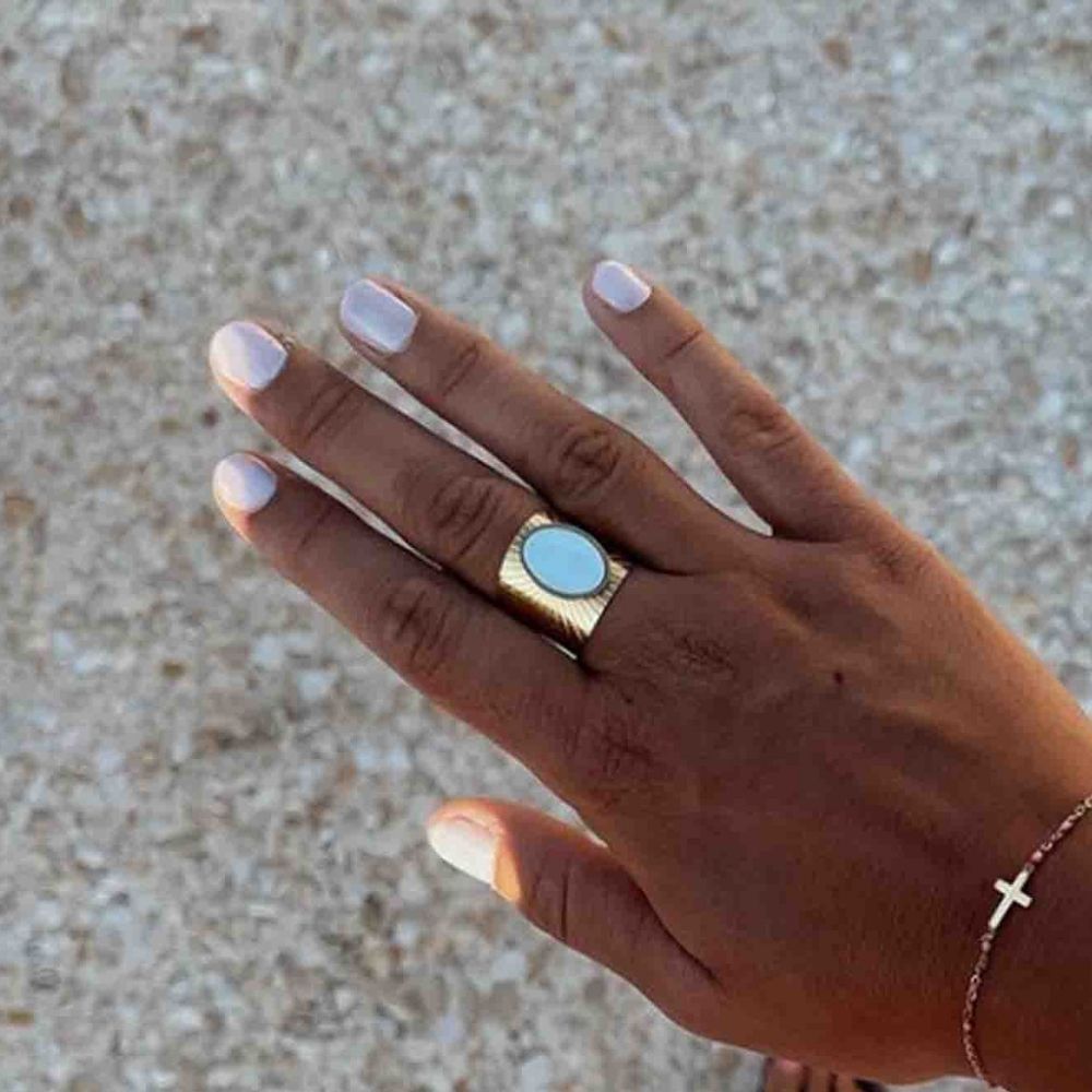 Hand met lichtgrijs gelakte nagels. Gouden ring met blauwe steen. Armband met kruis.