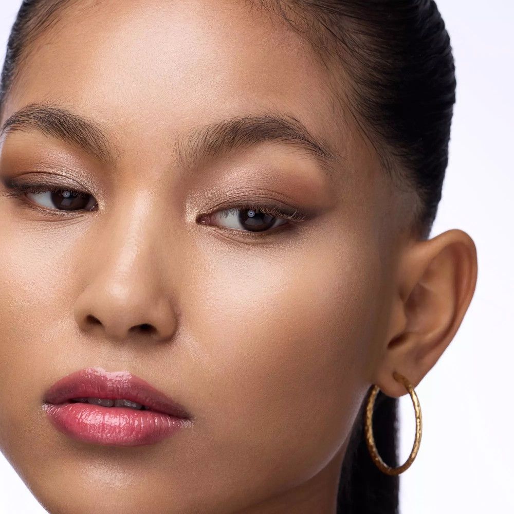 Gros plan d'un visage avec des créoles dorées. De l'ombre à paupières est appliquée sur les paupières.