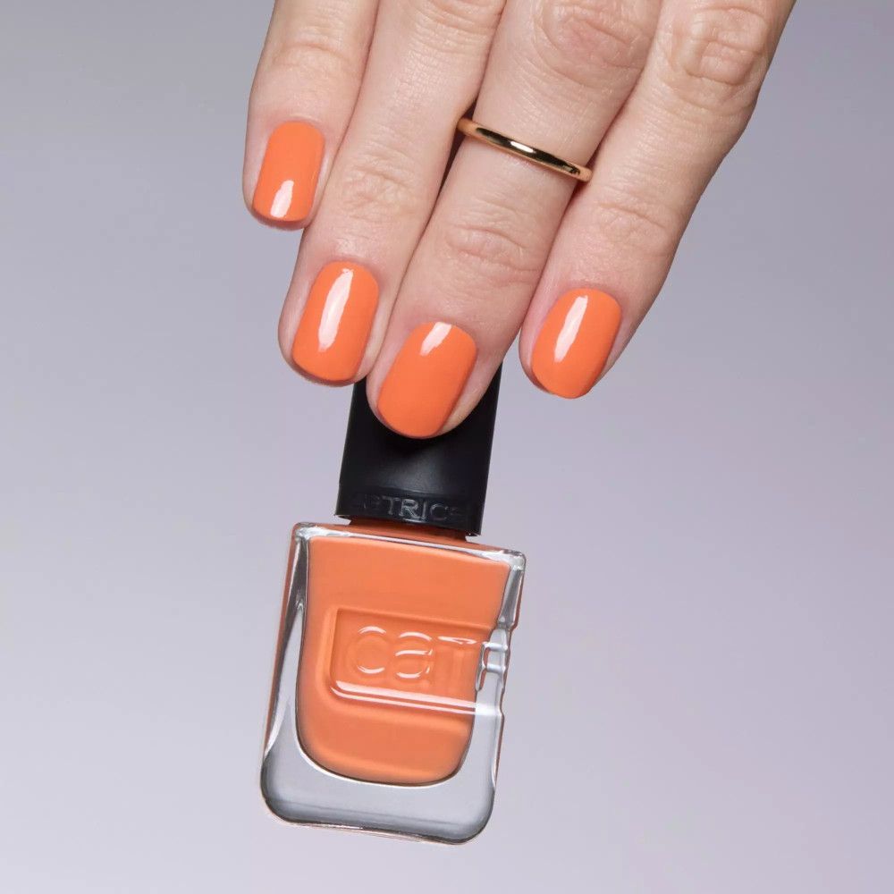 Main avec ongles vernis et flacon de vernis. Couleur : orange. Marque Catrice.