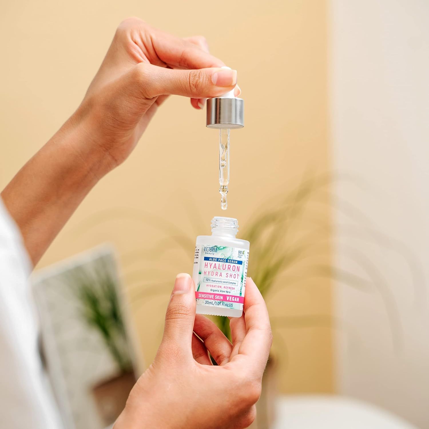 Hand houdt druppelaar boven Victoria Beauty Hyaluron Hydra Shot serumflesje.