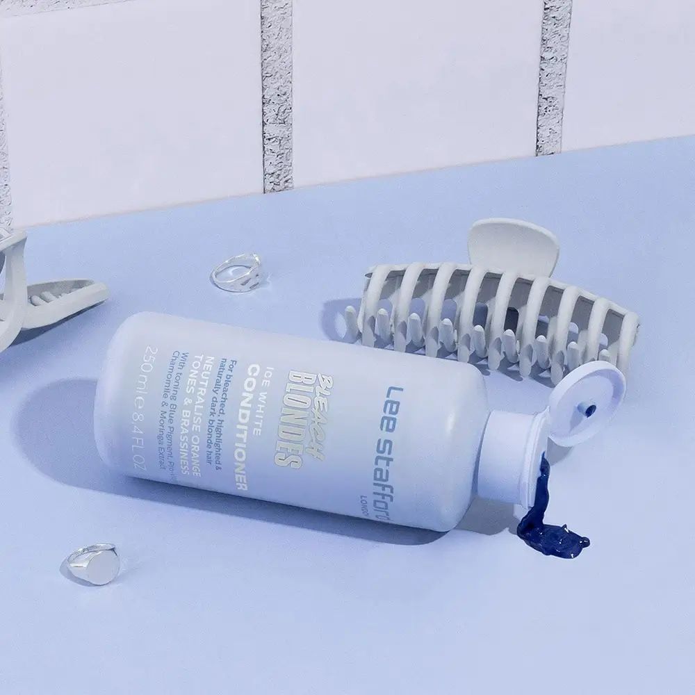 Lichtblauwe fles ligt. Haarclips en transparante accessoires ernaast. Product: LEE STAFFORD Bleach Blondes Conditioner.