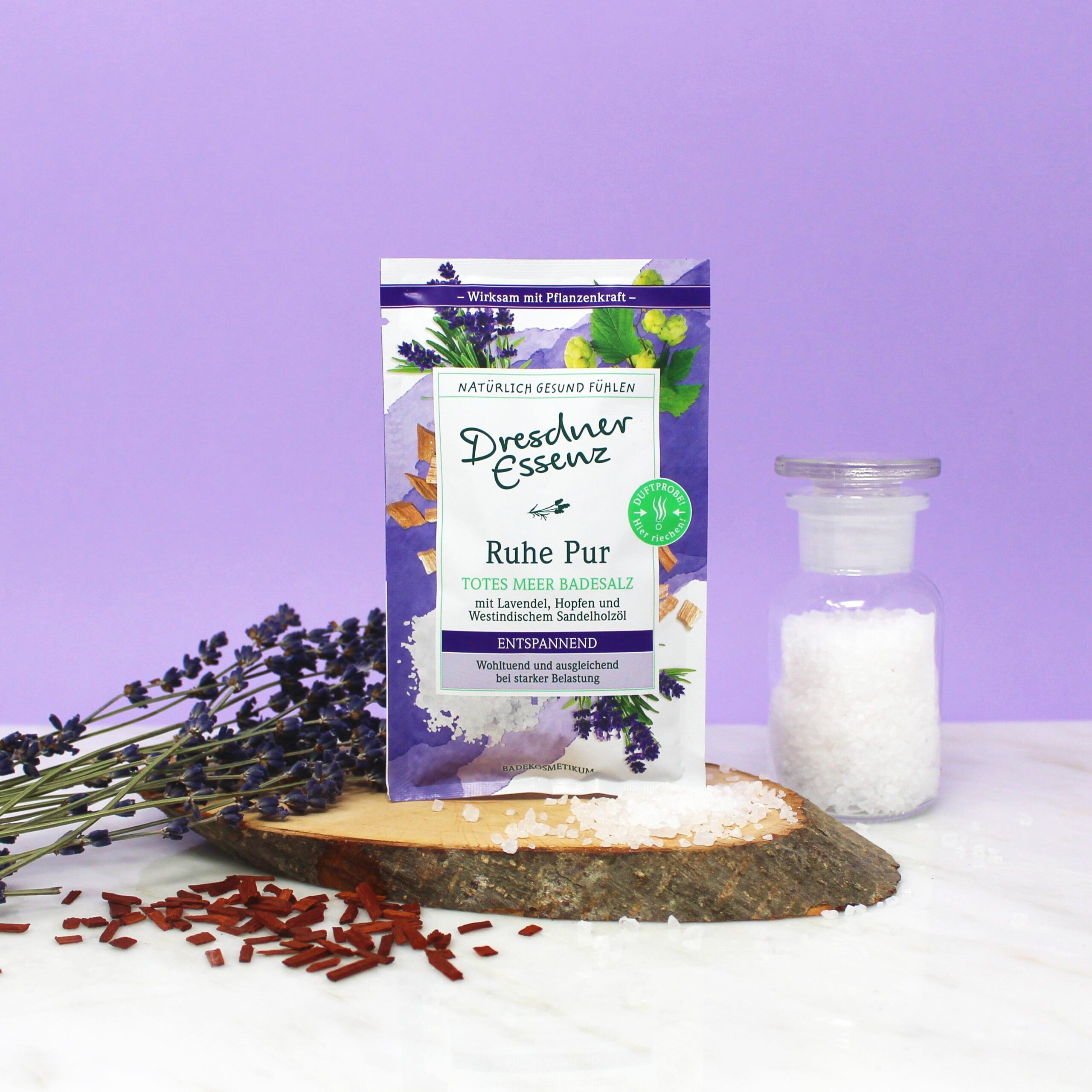 Sachet de sels de bain Dresdner Essenz Ruhe Pur sur une tranche de bois, à côté de lavande et d'un pot en verre.