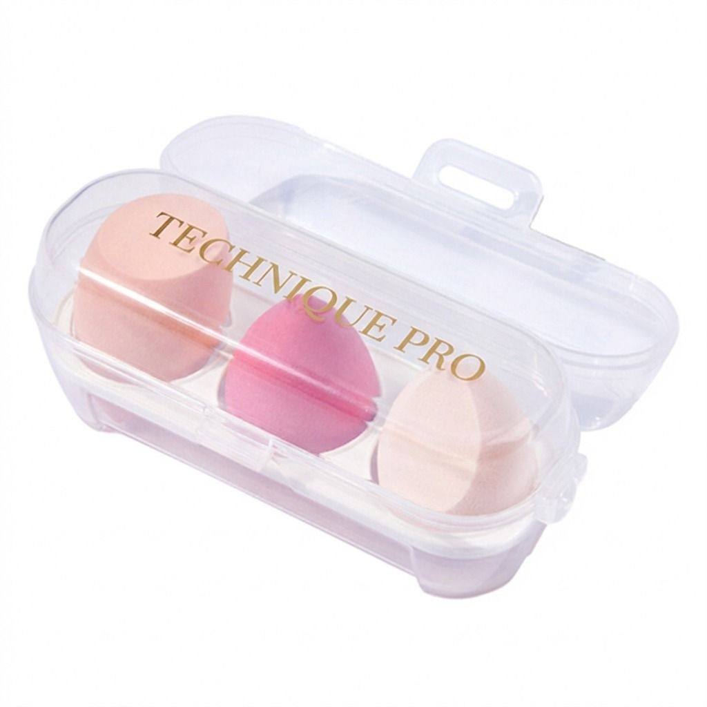Trois éponges de maquillage roses et pêche dans un étui de voyage transparent avec "TECHNIQUE PRO" écrit dessus.