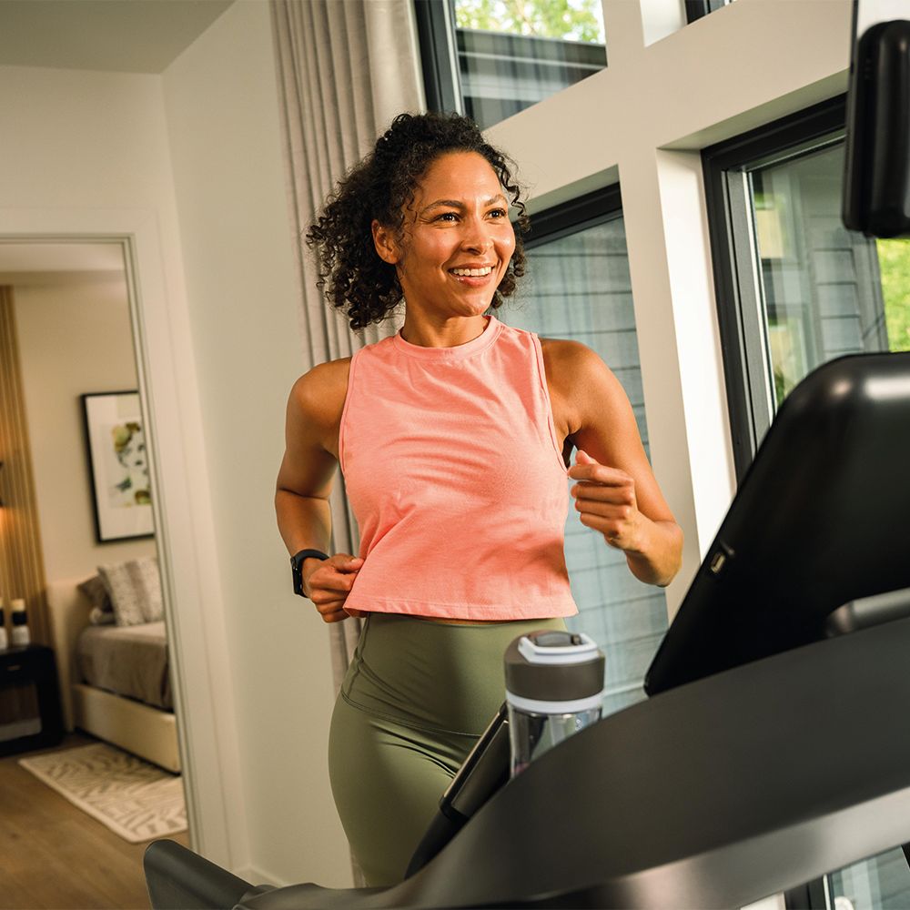 Vrouw die op een loopband rent. Ze draagt sportkleding en houdt een waterfles vast.
