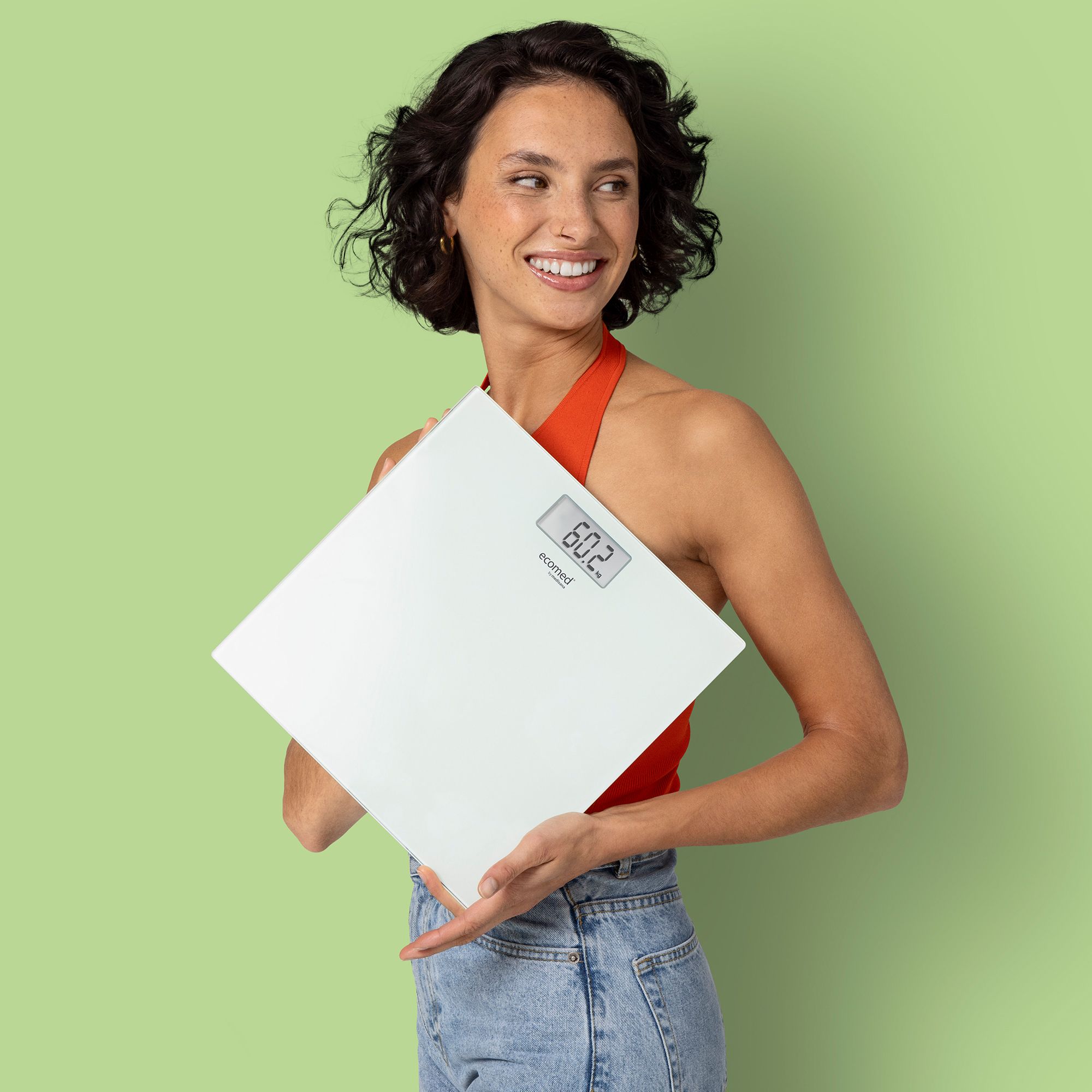 Une femme tient une balance personnelle blanche en verre avec affichage numérique (60.2 kg).