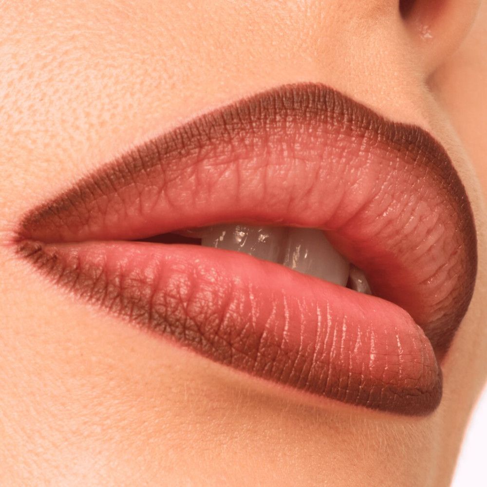 Gros plan sur des lèvres, bordées d'un crayon à lèvres brun. Bouche légèrement ouverte.