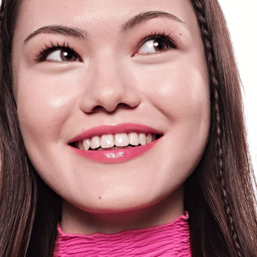 Portret van een vrouw met glanzende lippen. Ze draagt roze kleding en heeft vlechten.