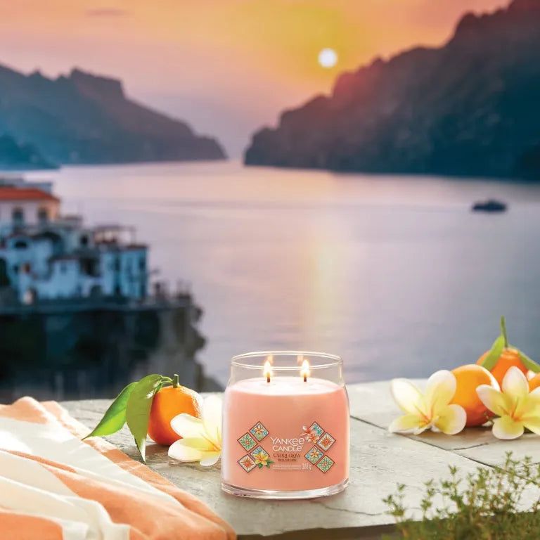 Yankee Candle Capri Glow. Bougie rose à deux mèches. Autocollant avec motifs floraux. Arrière-plan : mer, montagnes, coucher de soleil.