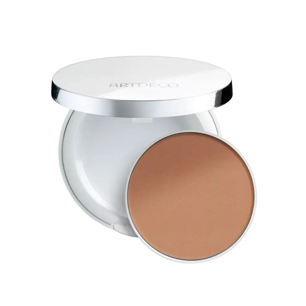 Poudre compacte blanche, bord argenté, ouverte. Recharge de poudre brune à côté. Couvercle avec inscription ARTDECO.