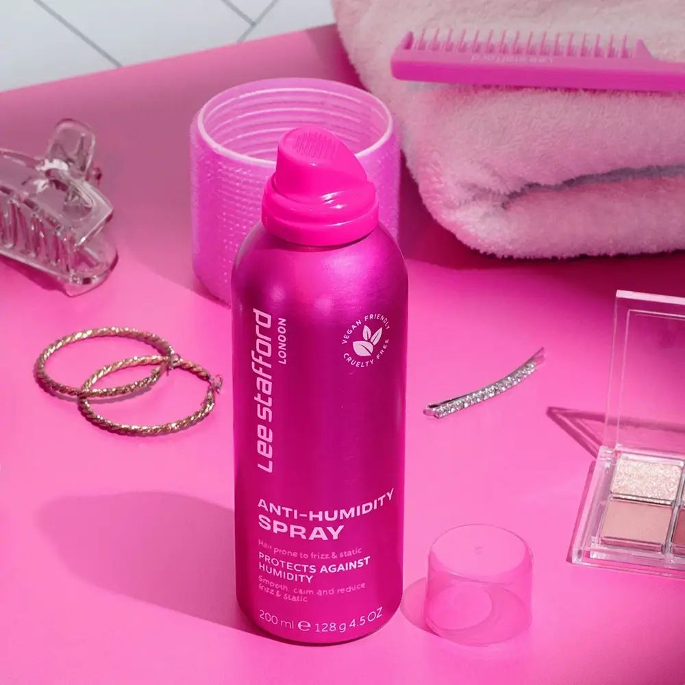 Roze spuitfles met accessoires. Opschrift: Lee Stafford London, Anti-Humidity Spray, Vegan, Cruelty Free. Accessoires: borstel, haarspelden, sieraden.