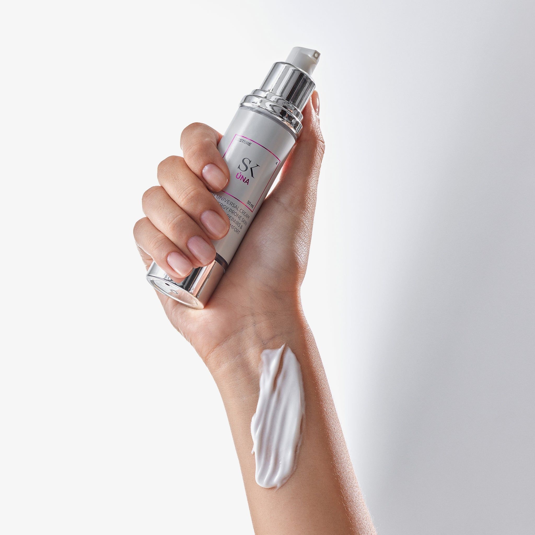 Hand houdt crèmefles vast. Klodder crème op de rug van de hand. Opschrift: SK Úna. Crème wit.