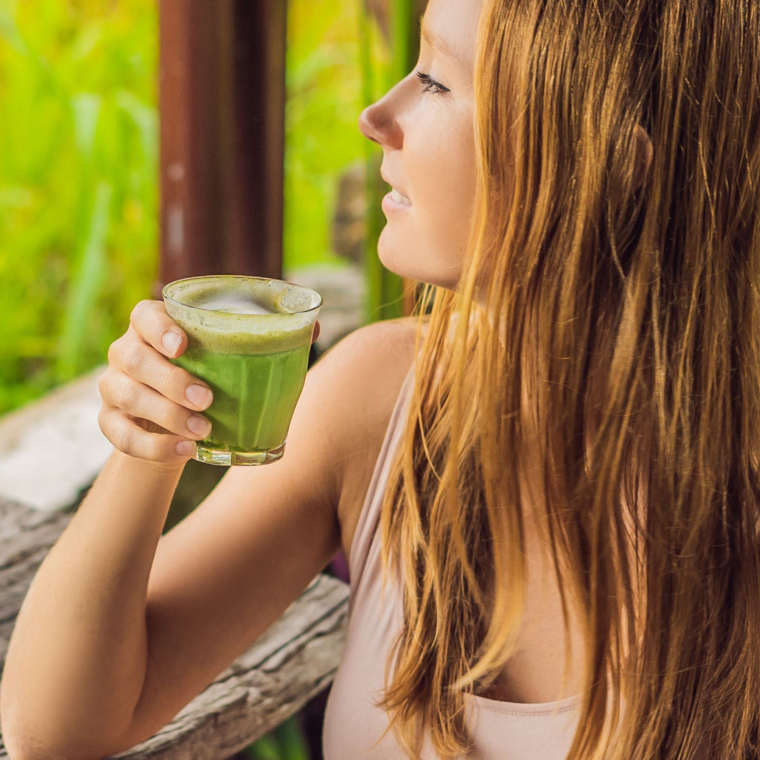 Een vrouw houdt een glas matcha thee vast. De thee is groen en in een glas. De vrouw is in profiel te zien.